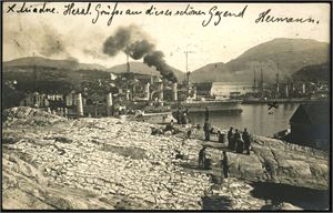 Kristiansund. Fotokort med klippfisk i forgrunnen og flere store krigsskip i bakgrunnen. Kortet med hjørnebrekk oppe til venstre. Brukt i 1906. K-3