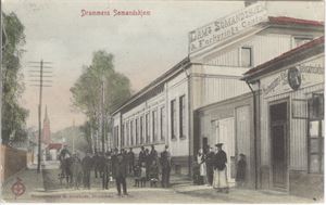 Drammen Sømandshjem (E.J.901) kolorert kort , mye folk i gata og reklame på butikker.  Stemplet 1912